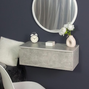 May include: A white ceramic mug with a black handle and the text "But First, Coffee" in a bold, black font. The mug is set against a blurred background, suggesting a cozy setting.