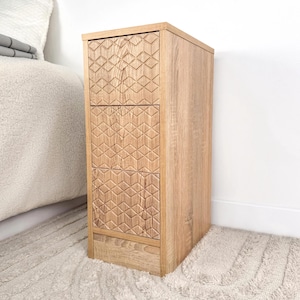 Könnte beinhalten: Ein Nachttisch aus hellem Holz mit drei Schubladen. Die Schubladen haben ein geometrisches Muster.