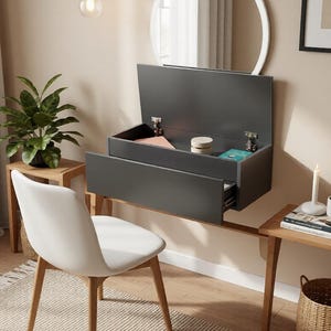 May include: A contemporary wall-mounted desk in a dark grey finish, featuring a drawer and a lift-up storage compartment. A white chair with wooden legs is positioned in front. A round mirror hangs above, with a small side table to the right.