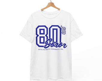 May include: White t-shirt with a blue graphic that says "80's Soror" and "Zeta Phi Beta Sorority, Inc."