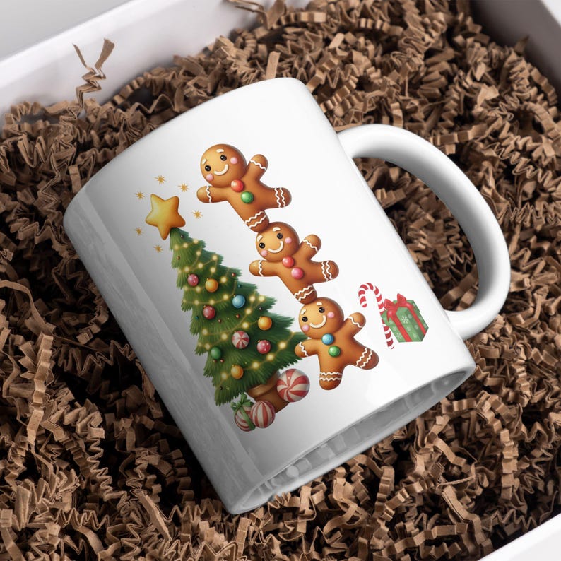 May include: White ceramic mug featuring a Christmas tree and gingerbread men design. The mug has a curved handle and is decorated with a star, candy canes, and a wrapped gift. The mug is placed in a white box with brown packing material.