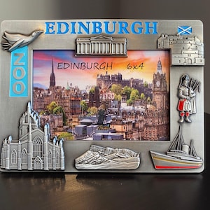 May include: A silver-coloured metal photo frame featuring embossed Edinburgh landmarks and text. The frame holds a 6x4 inch photo of the city, with decorative elements including a bird, a castle, and a bagpiper. The word "EDINBURGH" is displayed in blue.