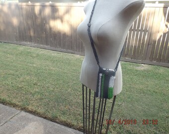 May include: Crocheted crossbody phone bag in shades of gray, white, and green. The bag has a long strap and a button closure. The bag is displayed on a mannequin.