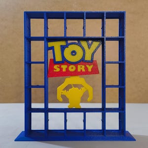 May include: A blue, grid-like shelf with the words "TOY STORY" in yellow and red. A yellow character is featured below the text. The shelf is a 3D-printed item, likely for displaying small toys or collectibles.