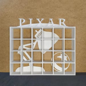 Può includere: Scaffale in legno bianco con 16 scomparti quadrati. Lo scaffale ha un ritaglio della lampada Pixar e la parola "PIXAR" in alto.