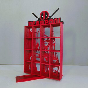 May include: Red and black 3D printed display stand with 16 compartments and a Deadpool character cutout. The stand has the word "DEADPOOL" printed on the top.