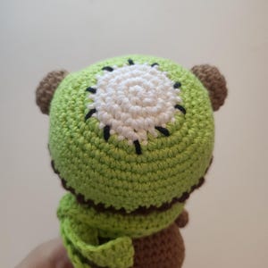 May include: A handmade crochet kiwi fruit plush toy. The toy features a green exterior with a white and black center, brown ears, and a brown body. The plush is soft and detailed, perfect for a child's toy or a unique decorative item.