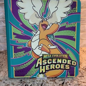 May include: A rectangular trading card binder featuring a vibrant graphic of a winged orange dragon-like creature. The background displays purple and green radial patterns with dots. The text reads MEGA EVOLUTION ASCENDED HEROES in bold letters.