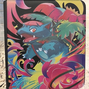 以下が含まれることがあります： フシギバナの鮮やかな多色グラフィックイラストが描かれた長方形のトレーディングカードバインダー。黒い背景に、背中に大きな植物の球根を乗せた青い生き物が描かれており、ピンク、黄色、緑の様式化された葉が周囲を囲んでいます。