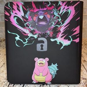 May include: A black rectangular binder featuring a graphic of a dark purple creature with red eyes surrounded by pink and teal energy, a grey padlock icon in the center, and a pink Slowpoke character with a blue shell on its tail at the bottom.