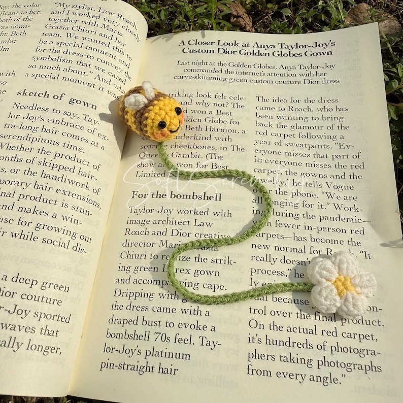 Puede incluir: Marcap&aacute;ginas de abeja de ganchillo con tallo verde y margarita blanca. La abeja es amarilla y marr&oacute;n con una cara sonriente. El marcap&aacute;ginas est&aacute; en un libro abierto.