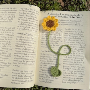 Puede incluir: Marcap&aacute;ginas de ganchillo hecho a mano con forma de girasol, con flor amarilla, centro marr&oacute;n, tallo y hoja verdes, sobre un libro abierto. Un accesorio de lectura.