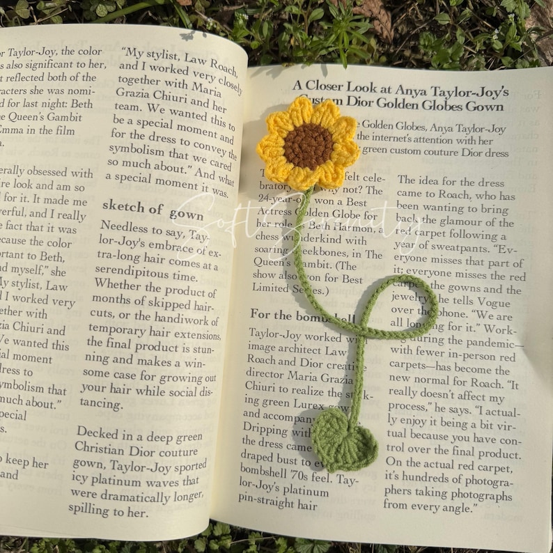 Puede incluir: Marcap&aacute;ginas de ganchillo hecho a mano con forma de girasol, con flor amarilla, centro marr&oacute;n, tallo y hoja verdes, sobre un libro abierto. Un accesorio de lectura.