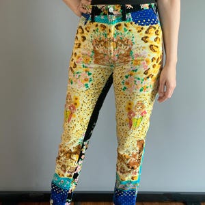 Peut inclure: Jean taille haute &agrave; motifs avec un design patchwork unique. Le jean pr&eacute;sente une base jaune avec des motifs floraux, l&eacute;opard et chats. Des patchs de tissu bleu et noir sont int&eacute;gr&eacute;s. Port&eacute; avec un haut noir.