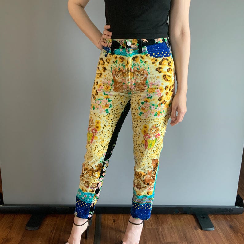 Peut inclure: Jean taille haute &agrave; motifs avec un design patchwork unique. Le jean pr&eacute;sente une base jaune avec des motifs floraux, l&eacute;opard et chats. Des patchs de tissu bleu et noir sont int&eacute;gr&eacute;s. Port&eacute; avec un haut noir.