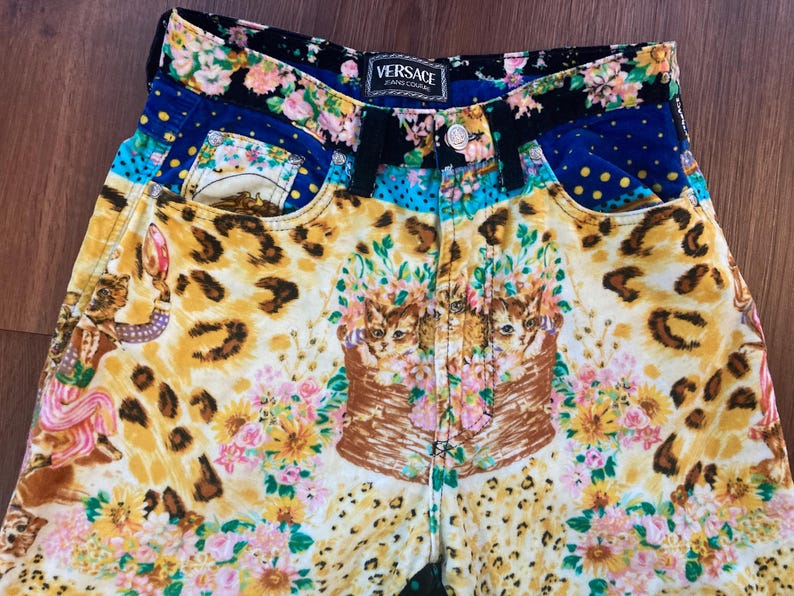 Peut inclure: Pantalon en jean Versace Jeans Couture au design vibrant et &eacute;clectique. Le pantalon pr&eacute;sente un m&eacute;lange de motifs, notamment un imprim&eacute; l&eacute;opard, des compositions florales et un motif de chat. La taille porte une &eacute;tiquette Versace.