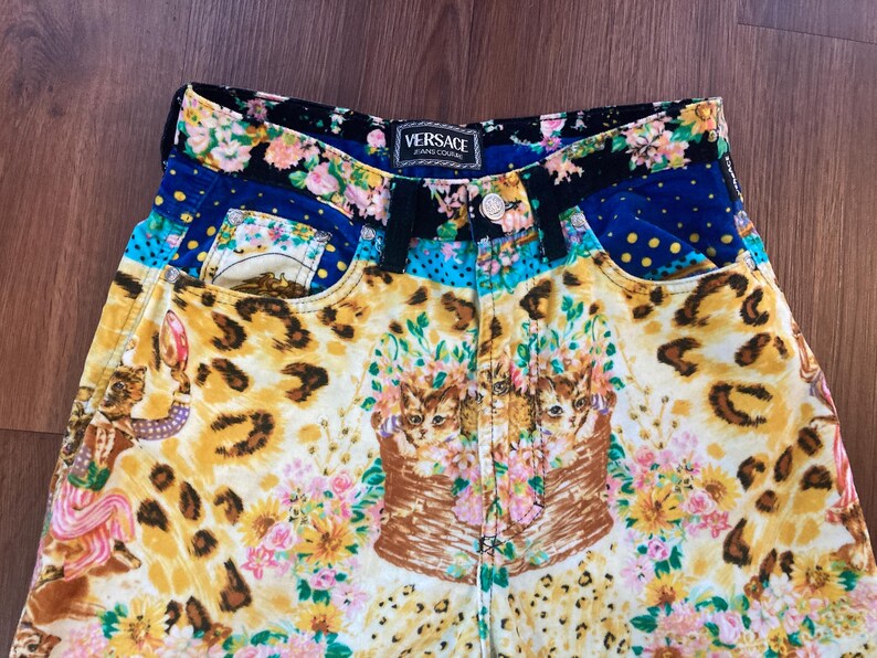 Peut inclure: Short en jean Versace Jeans Couture au design vibrant et &eacute;clectique. Le short pr&eacute;sente un m&eacute;lange de motifs, notamment des imprim&eacute;s l&eacute;opard, des compositions florales et des illustrations de chats. La ceinture et les poches ont des motifs floraux et &agrave; pois contrast&eacute;s.