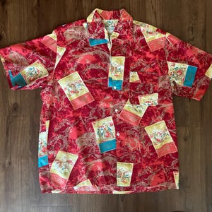 May include: A short-sleeved button-down shirt with a vibrant red and pink pattern. The shirt features rectangular patches with illustrations and teal accents. The collar and cuffs have a yellow trim. The shirt is made of a lightweight fabric.