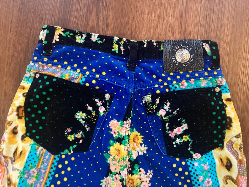 Peut inclure: Gros plan sur l'arri&egrave;re d'un jean Versace color&eacute;. Le jean pr&eacute;sente un motif patchwork avec des motifs floraux, &agrave; pois et animaliers. Un patch en cuir noir avec le logo Versace Jeans Couture est visible.