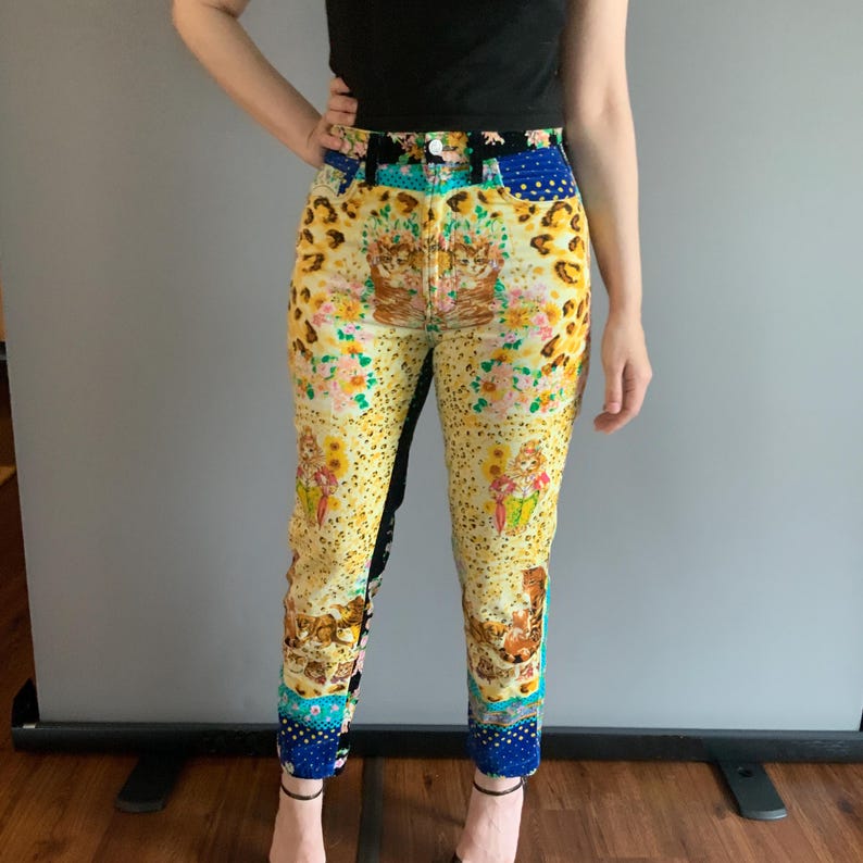 Peut inclure: Jean taille haute &agrave; motifs avec un design unique. Le jean pr&eacute;sente une base jaune avec un imprim&eacute; l&eacute;opard, des motifs floraux et des illustrations. Des pi&egrave;ces de tissu bleu et noir sont int&eacute;gr&eacute;es au design.