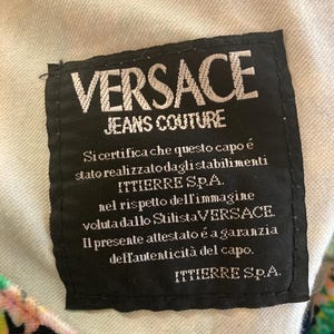 Peut inclure: &Eacute;tiquette noire avec texte blanc "VERSACE JEANS COUTURE". Le texte italien certifie l'authenticit&eacute; du v&ecirc;tement, avec le logo ITTIERRE S.p.A. L'&eacute;tiquette est cousue sur un tissu de couleur claire.