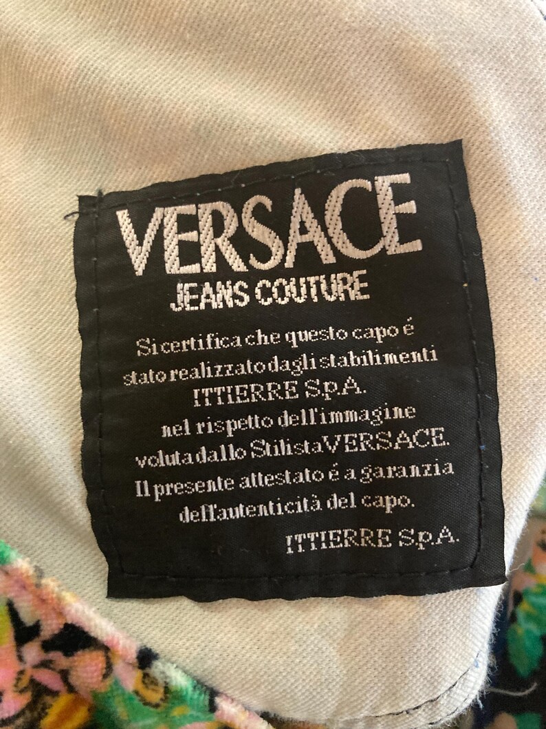 Peut inclure: &Eacute;tiquette noire avec texte blanc "VERSACE JEANS COUTURE". Le texte italien certifie l'authenticit&eacute; du v&ecirc;tement, avec le logo ITTIERRE S.p.A. L'&eacute;tiquette est cousue sur un tissu de couleur claire.