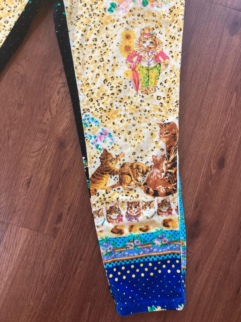 Peut inclure: Un pantalon &agrave; motifs avec un motif de chat fantaisiste. Le pantalon a un fond jaune &agrave; imprim&eacute; l&eacute;opard avec diverses illustrations de chats, des accents floraux et une bordure &agrave; pois bleus. Le pantalon est fait d'une mati&egrave;re douce et confortable.