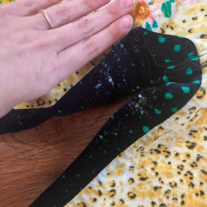 Peut inclure: Tissu noir &agrave; pois verts et motif floral jaune et blanc. Le tissu est tenu par une main avec une bague en or. Le tissu pr&eacute;sente un motif l&eacute;opard.