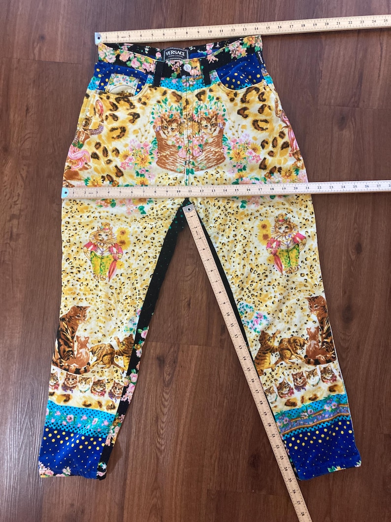 Peut inclure: Jean taille haute avec un motif vibrant. Le jean pr&eacute;sente un m&eacute;lange d'imprim&eacute; l&eacute;opard, de motifs floraux et de chats. La ceinture porte le logo "Versace". La palette de couleurs comprend le jaune, le bleu, le noir et le rose.