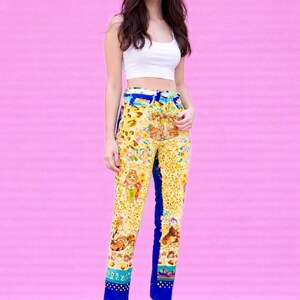 Peut inclure: Une femme porte un haut court blanc et un pantalon &agrave; motifs jaunes avec des accents bleus. Le pantalon pr&eacute;sente un imprim&eacute; floral et animalier color&eacute;. Elle porte &eacute;galement des talons bleus. Le fond est rose uni.