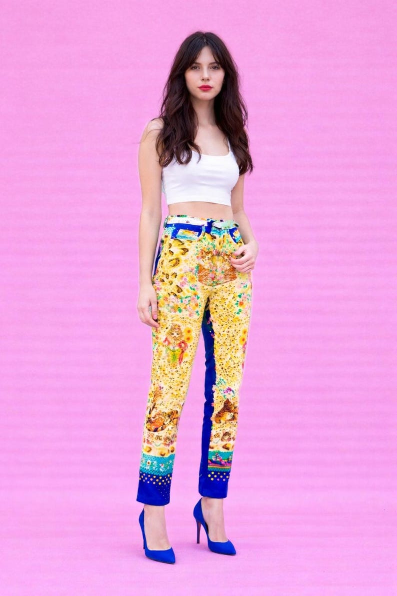 Peut inclure: Une femme porte un haut court blanc et un pantalon &agrave; motifs jaunes avec des accents bleus. Le pantalon pr&eacute;sente un imprim&eacute; floral et animalier color&eacute;. Elle porte &eacute;galement des talons bleus. Le fond est rose uni.