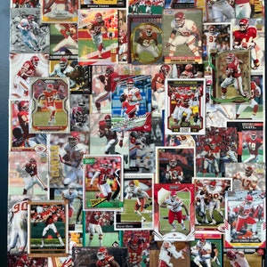 May include: A collage of Kansas City Chiefs football trading cards featuring various players, including Derrick Thomas, Patrick Mahomes, and Travis Kelce. The cards are in various colors and designs, with some featuring the team's logo and others featuring player photos.