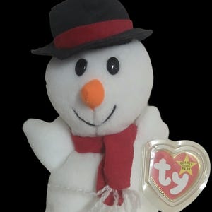 May include: A plush snowman toy with a black top hat, red scarf, and orange nose. The snowman has black button eyes and a stitched smile. A heart-shaped tag with the text "Beanie Babies" is attached.