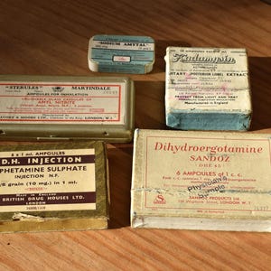 May include: An assortment of vintage pharmaceutical boxes, including "Sodium Amytal," "Sterules," "B.D.H. Injection," "Dihydroergotamine," and "Kudermycin." The boxes are in various sizes and colors, with text labels.