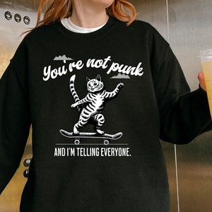 May include: Black sweatshirt with a white graphic of a cat skateboarding and the text "You're not punk and I'm telling everyone."
