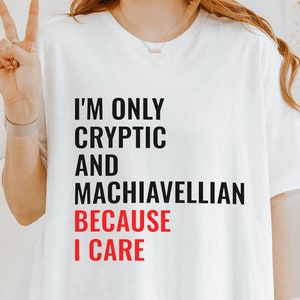 May include: White t-shirt with black text that reads "I'm only cryptic and Machiavellian because I care". The word "care" is in red.