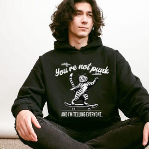 May include: A black hoodie with a white graphic of a cat skateboarding and the text "You're not punk and I'm telling everyone."