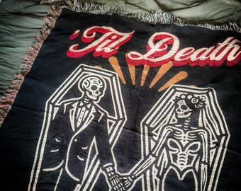 Puede incluir: Tapiz tejido negro con un contorno blanco de dos esqueletos que se toman de la mano en ataúdes. Los esqueletos están vestidos con un esmoquin y un vestido de novia. El texto "Til Death" está escrito en rojo y blanco sobre los esqueletos.