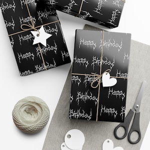 May include: Black gift boxes wrapped in paper with "Happy Birthday" text in white, tied with twine and adorned with white star and heart-shaped tags. A ball of twine, scissors, and blank tags are also present.