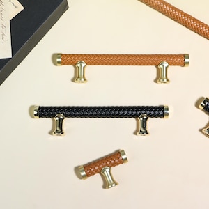 May include: A collection of cabinet pulls with a woven leather design. The pulls are available in brown and black, with gold-colored accents. The cabinet pulls are in various sizes and shapes, with a T-bar design.