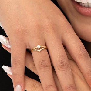 May include: A gold ring with a small, clear gemstone set in the center. The ring is designed with a V-shaped band.