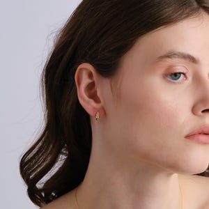 Puede incluir: Primer plano de la oreja de una persona con un peque&ntilde;o aro de oro. El arete es simple y delicado, con un dise&ntilde;o ligeramente retorcido.