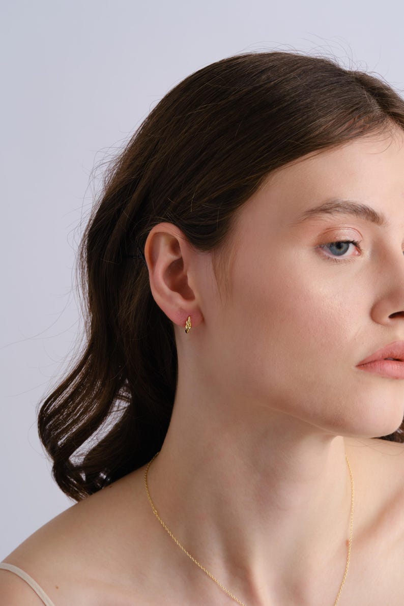 Puede incluir: Primer plano de la oreja de una persona con un peque&ntilde;o aro de oro. El arete es simple y delicado, con un dise&ntilde;o ligeramente retorcido.