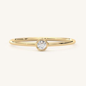 May include: A simple gold band ring with a single round bezel-set diamond.