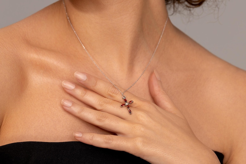 May include: A silver chain necklace with a red gemstone cross pendant.
