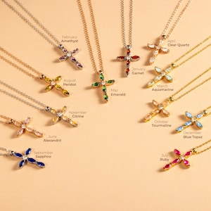 May include: Twelve gold necklaces with cross pendants, each featuring a different birthstone. The birthstones are amethyst, peridot, emerald, citrine, alexandrite, sapphire, ruby, clear quartz, aquamarine, tourmaline, blue topaz, and garnet.
