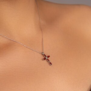 May include: A silver chain necklace with a red gemstone cross pendant.