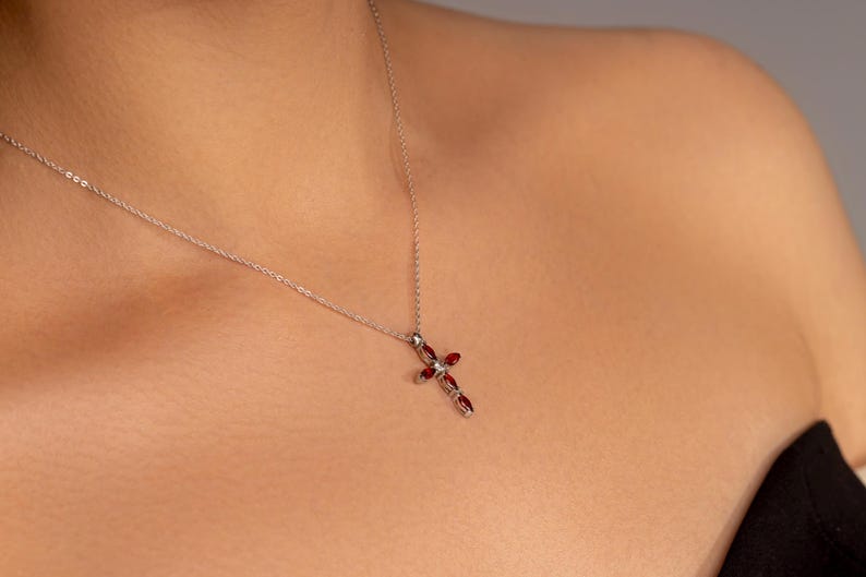 May include: A silver chain necklace with a red gemstone cross pendant.