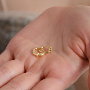 Puede incluir: Un par de pendientes de aro de oro con un dise&ntilde;o de nudo retorcido.