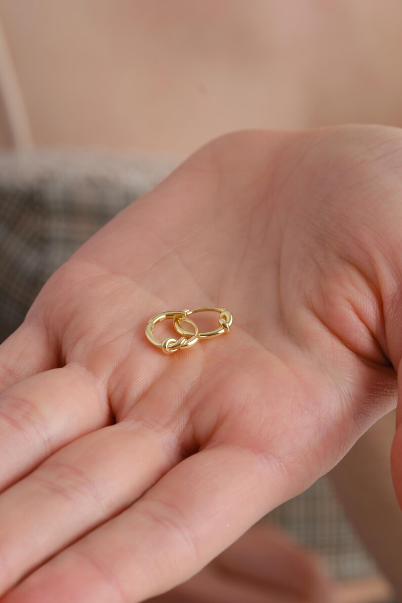 Puede incluir: Un par de pendientes de aro de oro con un dise&ntilde;o de nudo retorcido.